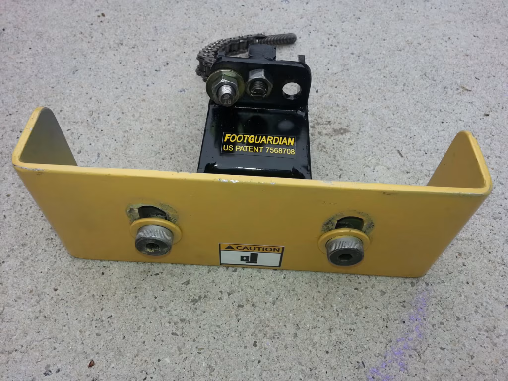 Yellow Footguardian pallet jack protector with black mounting bracket and chain. "CAUTION" sticker visible.